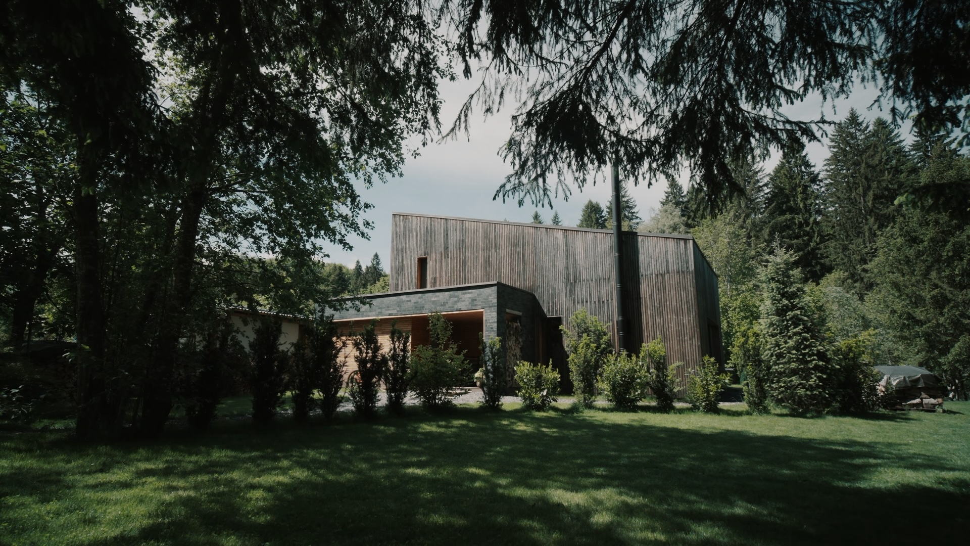 Exteriorul modern al 663A Mountain Chalet, cu fațadă din lemn vertical și piatră, situat într-o poiană însorită înconjurată de brazi înalți – locație izolată perfectă pentru workation.
