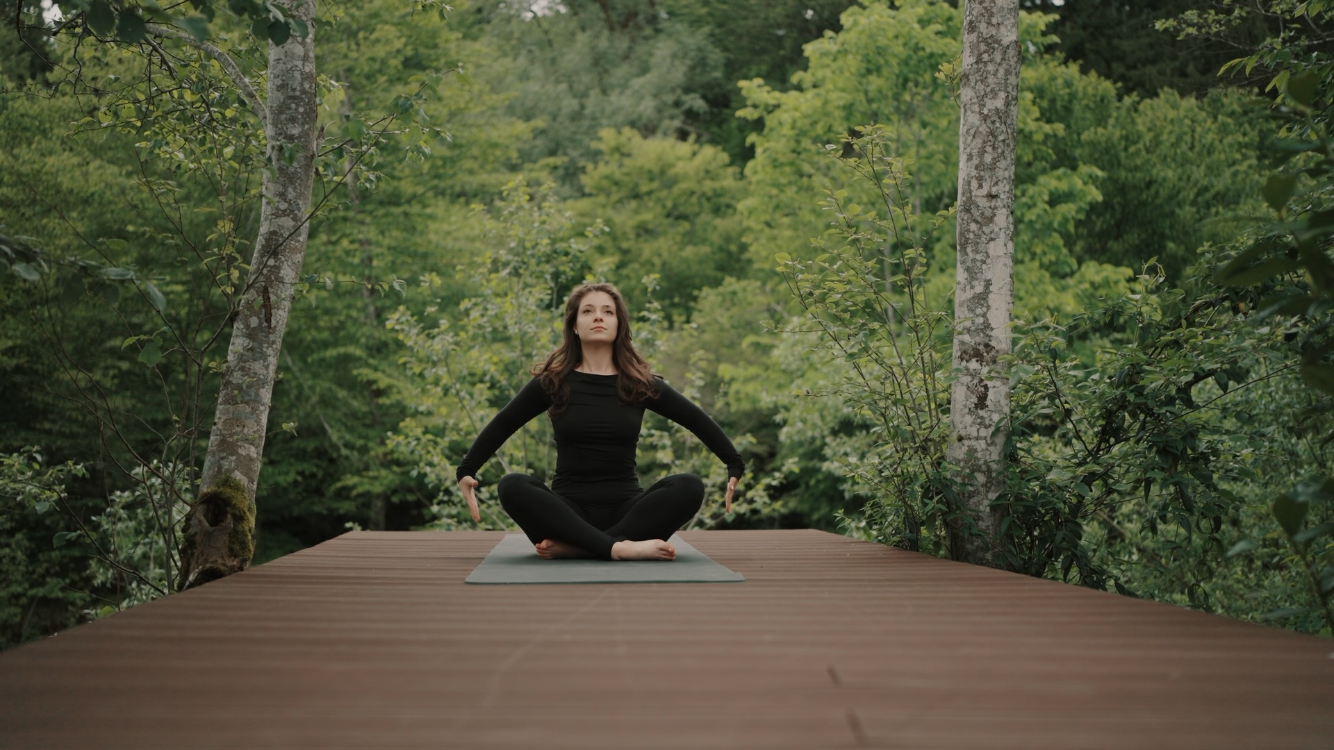 yoga-padure-deck-lemn-relaxare-dupa-munca-663a Femeie practicând yoga și meditație pe o platformă de lemn (deck) în mijlocul pădurii la 663A Mountain Chalet, înconjurată de verdeață densă.